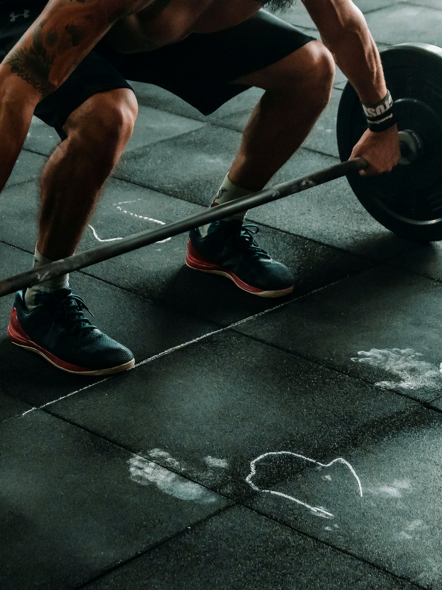 Person lifting a loaded barbell from rubber gym flooring.