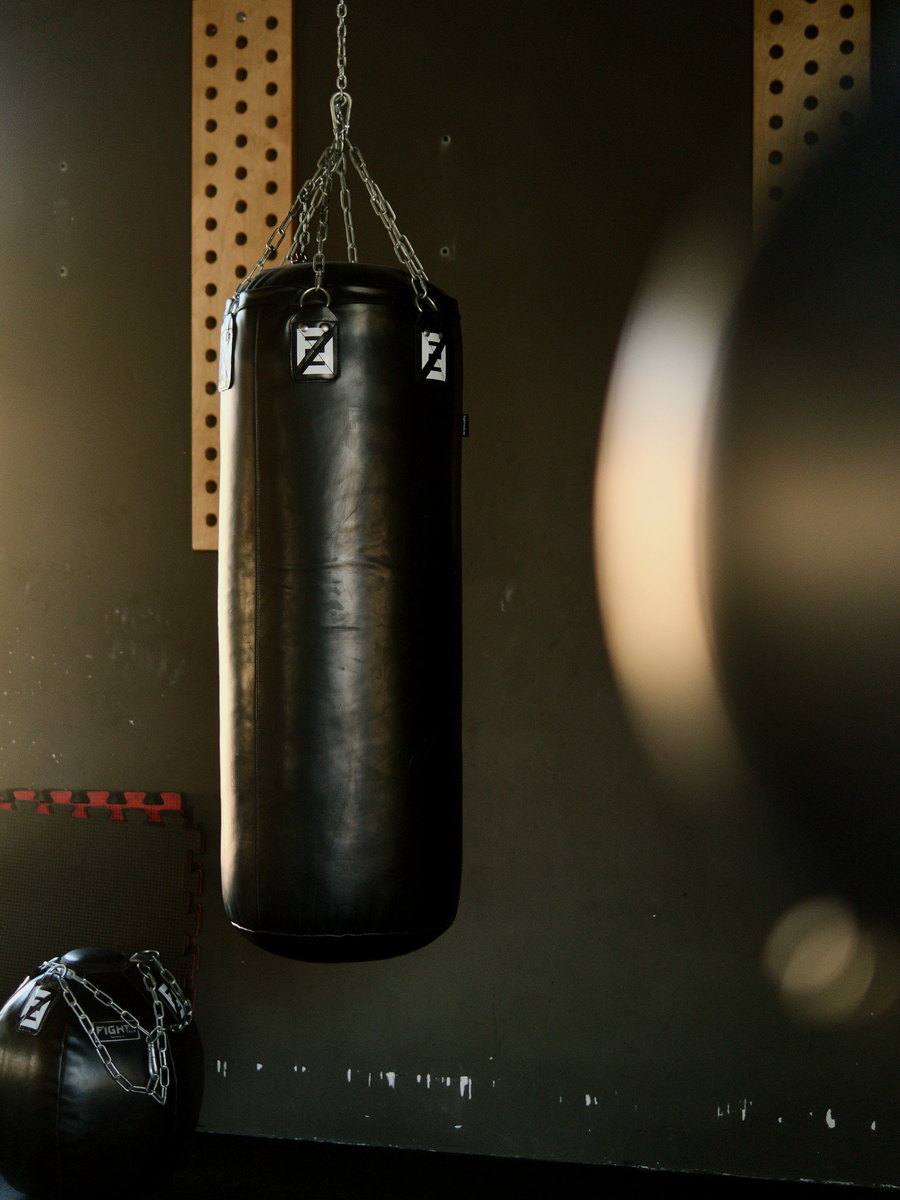 Black punch bag hanging on a chain in a gym, with a floor bag beside it.
